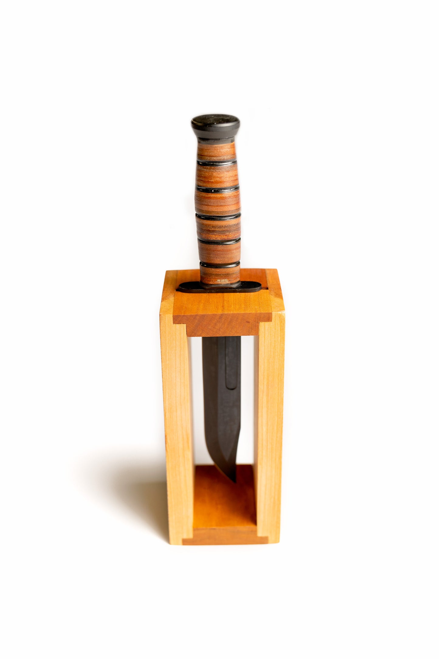 Personalized Ka-Bar knife display block made from solid cherry wood, shown holding a USMC fighting knife on a desk.