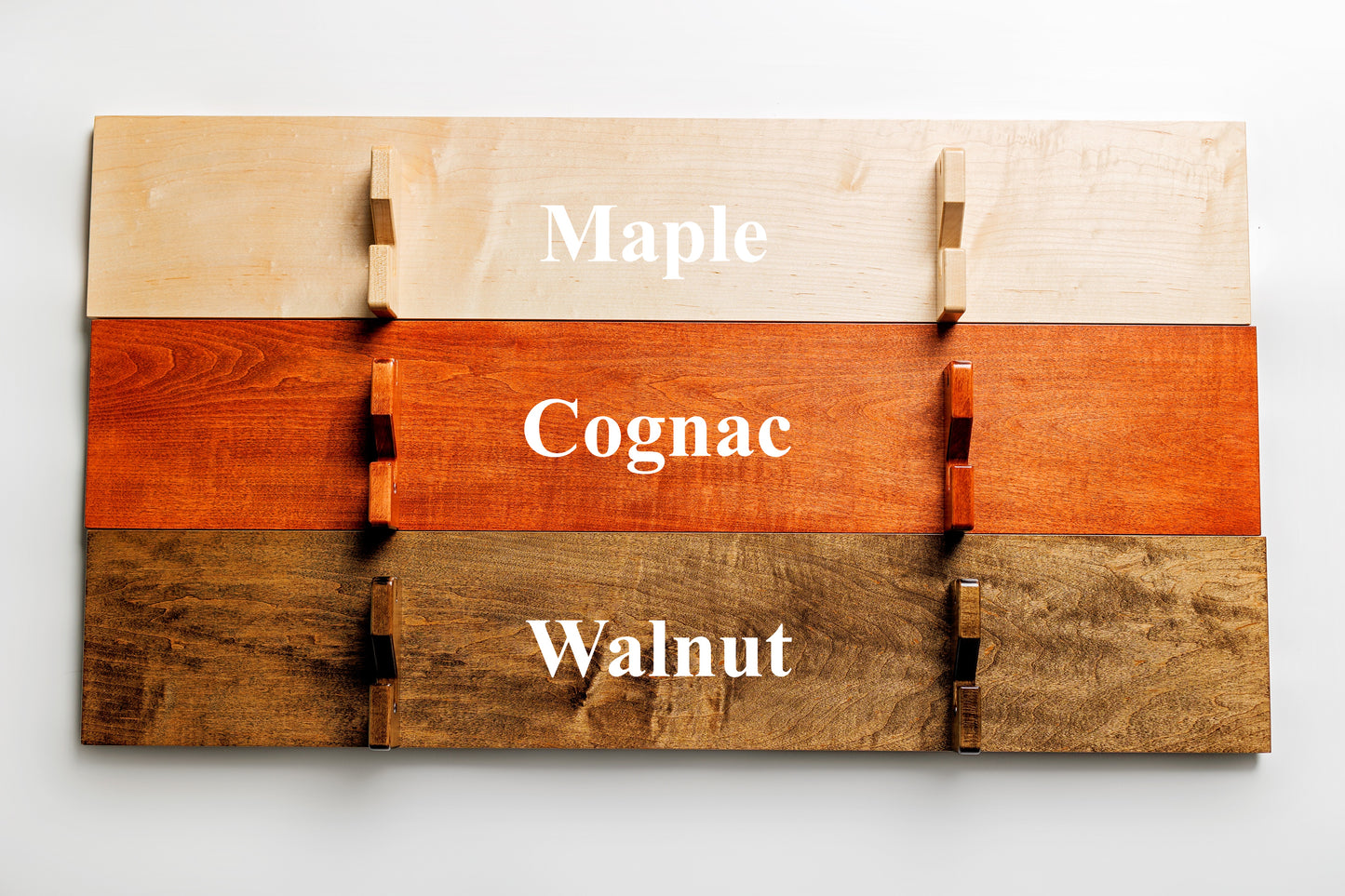 Three Universal Sword Displays showcasing the available hardwood finishes: light Maple, dark Walnut, and classic Cognac.